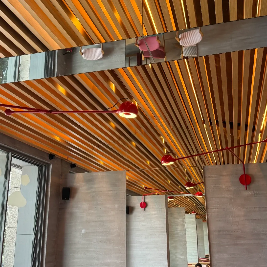 Red articulated lamps reaching across a slatted timber ceiling, doubled in a mirrored band