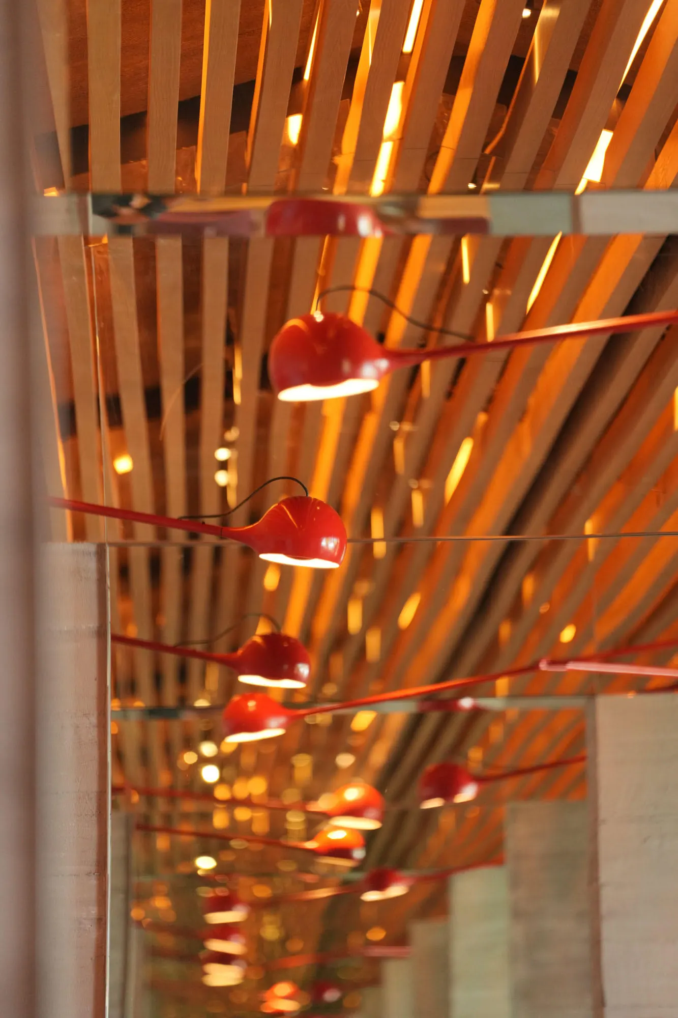 Red lamps on long arms reflected down a mirrored band beneath the slatted timber ceiling